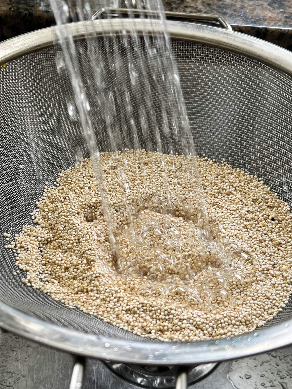 White quinoa being rinsed in a fine mesh sieve. 