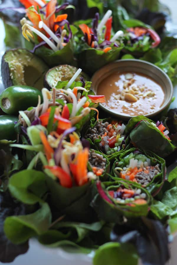 Plateful of raw summer green leaf wraps with noodles and spicy peanut ginger sauce.