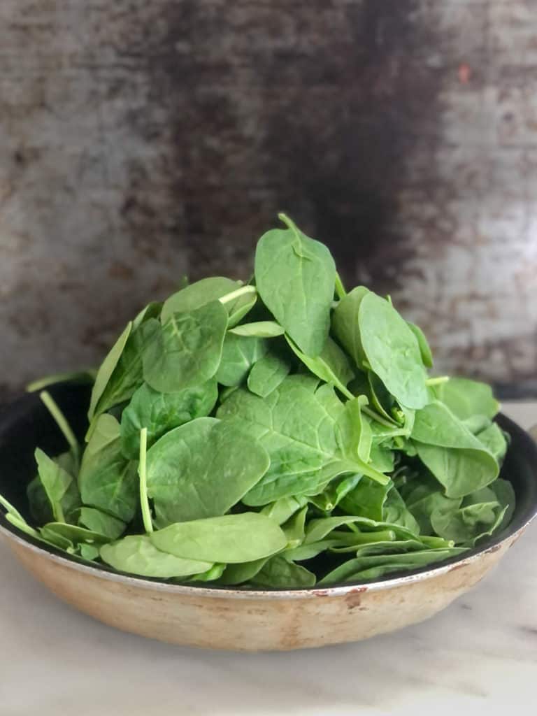 Large pile of raw spinach leaves in a skillet.
