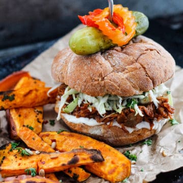 Vegan jackfruit burger with slaw surrounded by sweet potato fries.