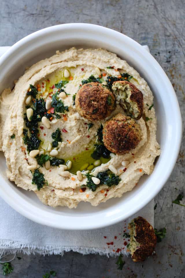 falafel balls sitting on chickpea hummus with a drizzle of oil and parsley