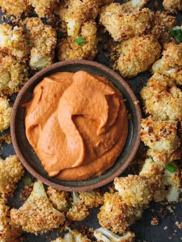 Cashew cream in a bowl surrounded by baked cauliflower nuggets.