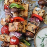 Skewers of tofu and vegetables with a bowl of dipping sauce.