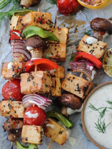 Skewers of tofu and vegetables with a bowl of dipping sauce.