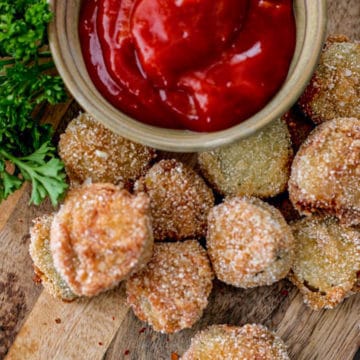 Fried pickled displayed on a cutting board with a bowl of spicy ketchup.