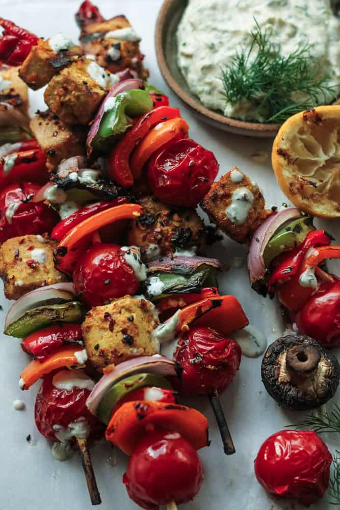 Tofu and vegetables skewers on a grilling pan with mushrooms, tomatoes and dipping sauce.