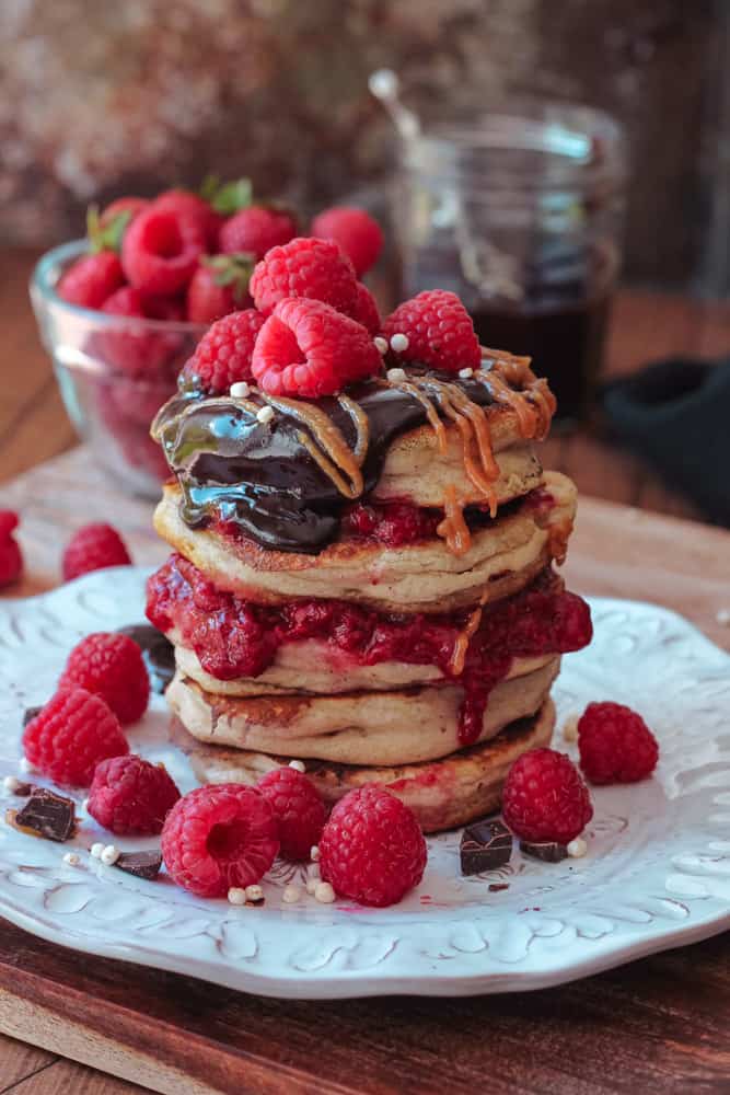 stack of vegan pancakes with chocolate ganache raspberries and maple peanut butter drizzle