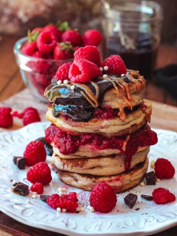 Stack of pancakes topped with fresh berries and chocolate ganache.