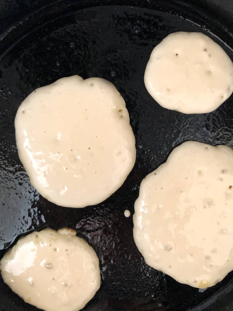 Four pancakes cooking in a hot skillet.