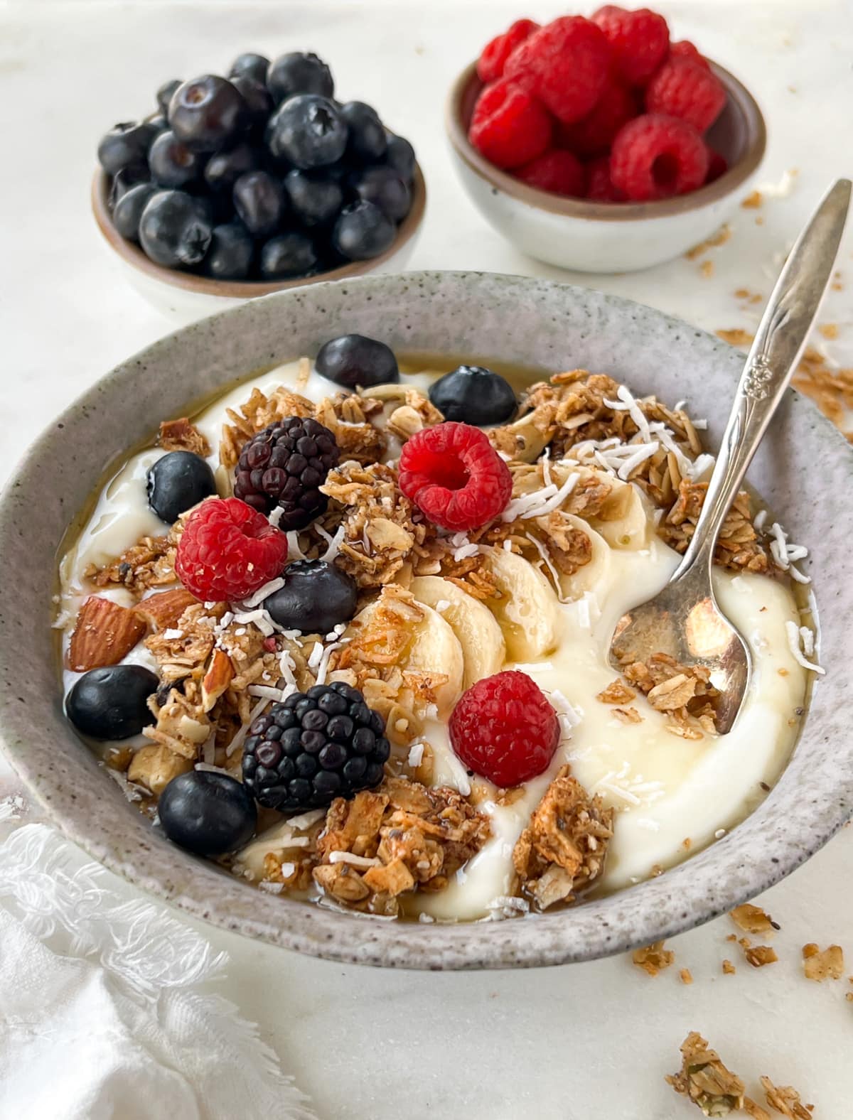 Yogurt granola berry breakfast bowl surrounded by bowls of raspberries and blueberries.