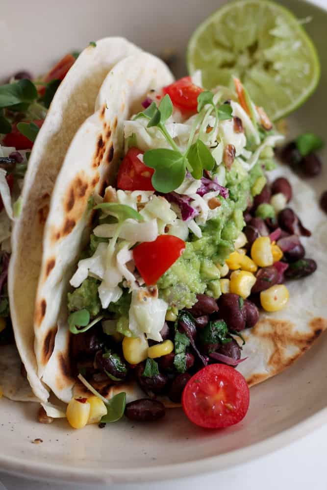 close up picture of a corn black beans avocado and tomato tacos in tortilla