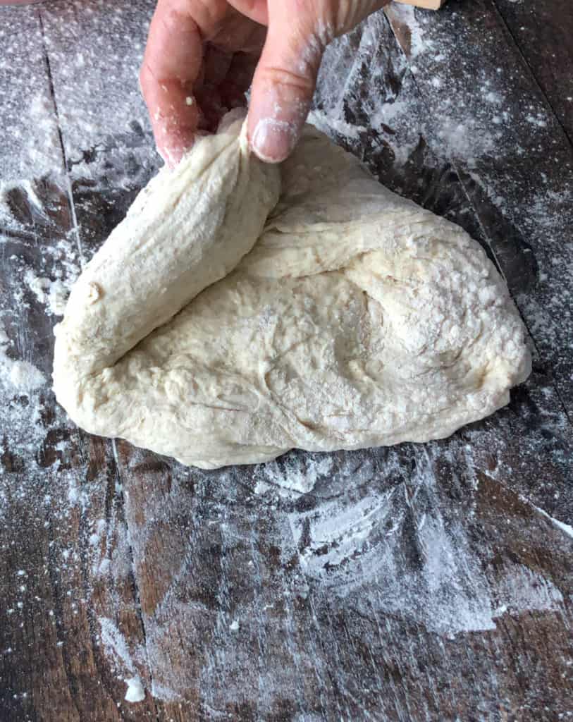 Bread dough on a floured surface being folded.