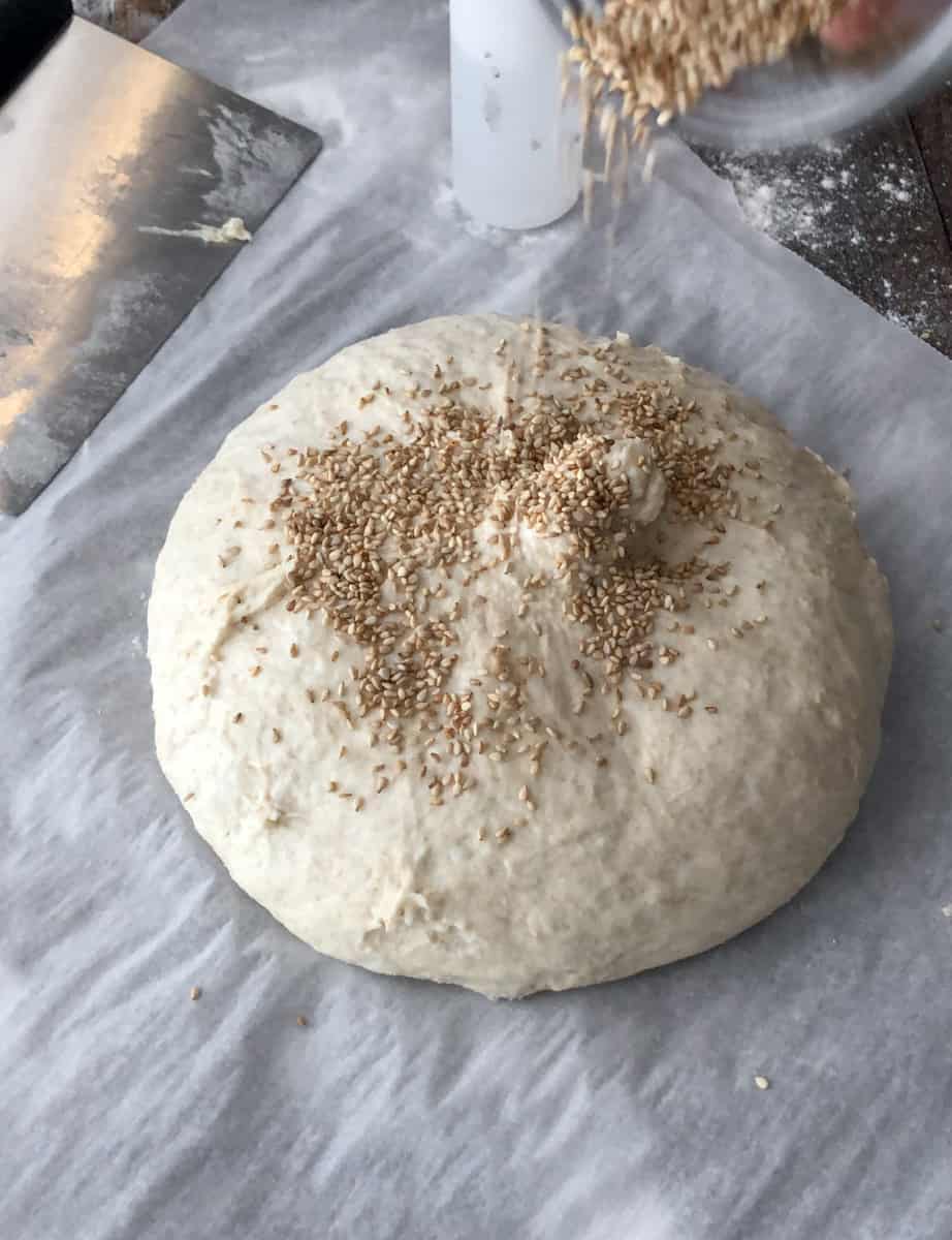 Sesame seeds being poured on top of bread dough before going into oven.