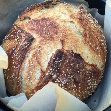 Freshly baked rustic bread surrounded by baking paper in a Dutch oven.