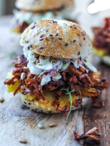 Spicy Pulled Jackfruit and creamy coleslaw served in a seedy slider bun sitting on a cutting board.