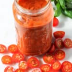 Jar of tomato passata surrounded by sliced cherry tomatoes and basil.