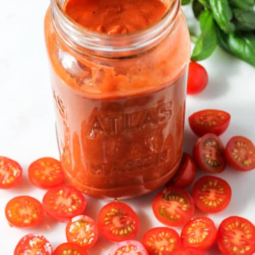 Jar of tomato passata surrounded by sliced cherry tomatoes and basil.