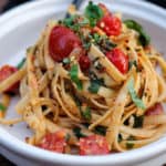 Large tangle of fettuccine with tomatoes and spinach on a plate.