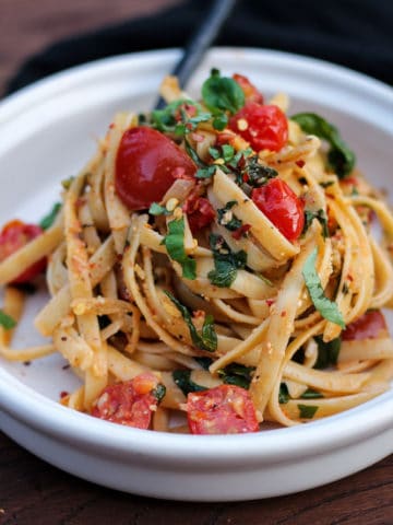 Large tangle of fettuccine with tomatoes and spinach on a plate.