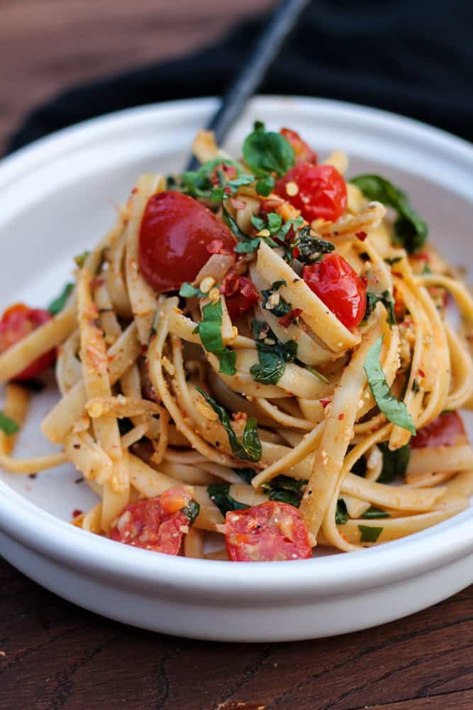 Large tangle of fettuccine with tomatoes and spinach on a plate.