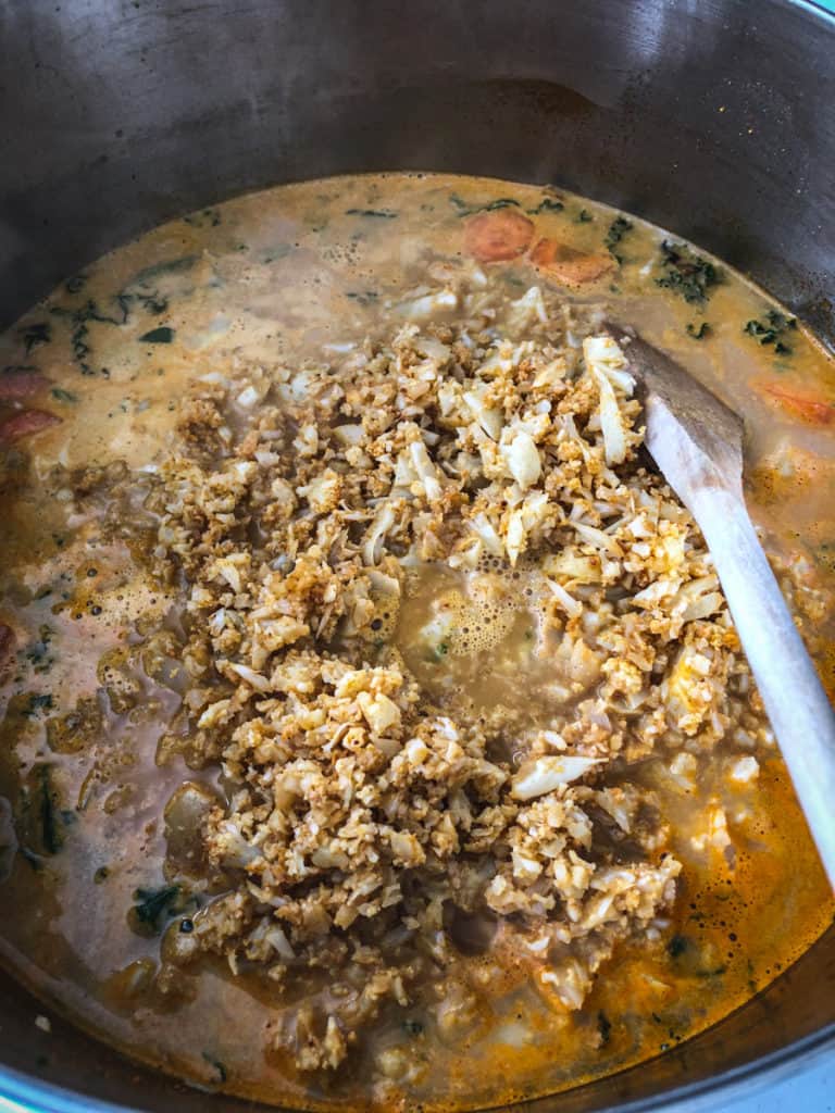 A pot of cauliflower rice soup being stirred with a wooden spoon.