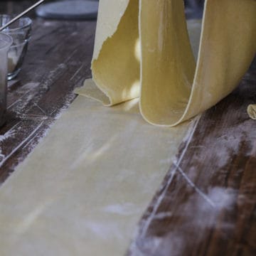 Sheets of homemade pasta being rolled through pasta machine.
