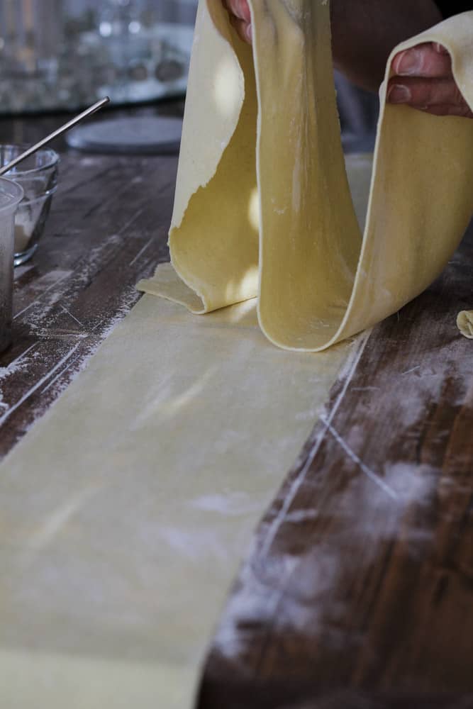 Sheets of homemade pasta being rolled through pasta machine.