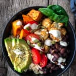 Vegan taco bowl with rice, beans, sweet potatoes, avocado and sauce drizzles.