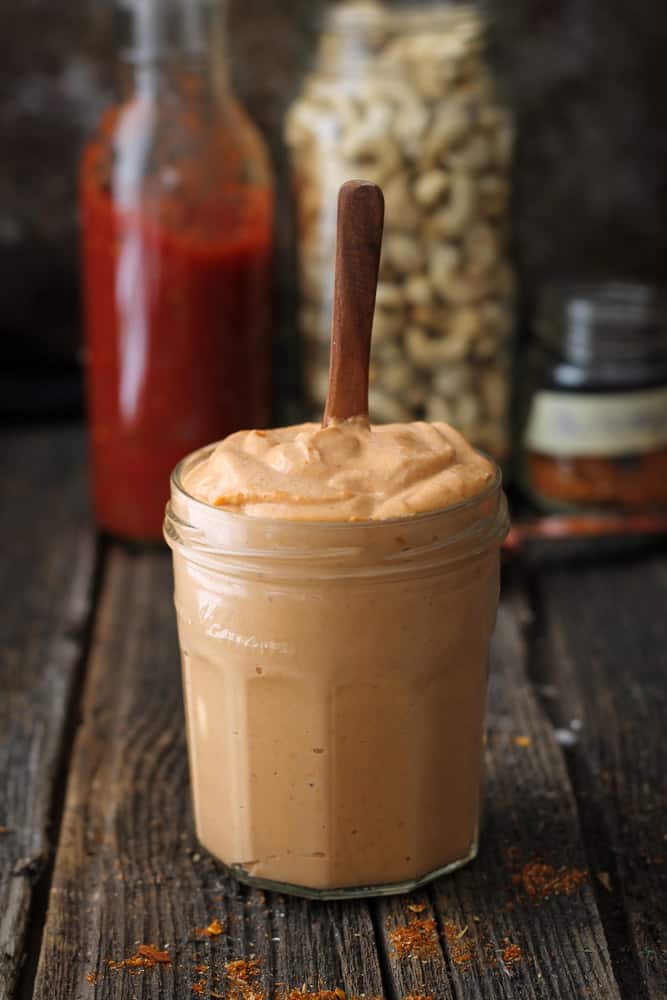 A jar of creamy tex-mex cashew sauce sitting on a cutting board/