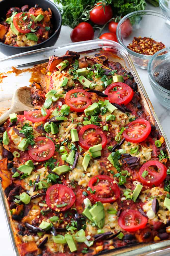 Vegan Tex-Mex Lasagna in a pan topped with avocado, onions, and tomato slices.