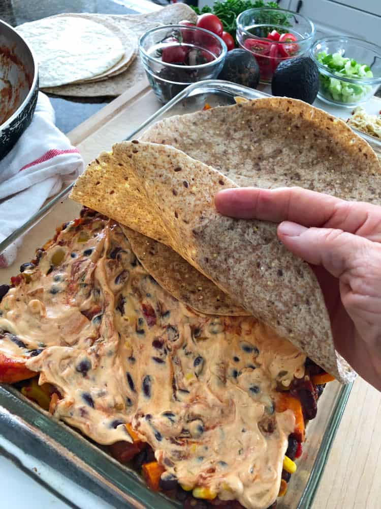 Tex-Mex Lasagna being layered in pan with tortilla and sauce.