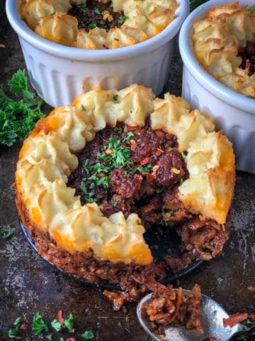 Vegan Shepherd's pie filling piped with mashed potatoes baked in individual mini pots.