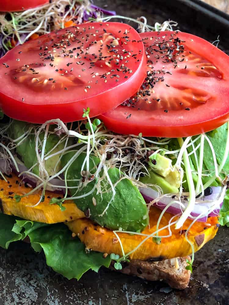 Open faced vegetable sandwich with sweet potato, tomato, avocado, and sprouts.