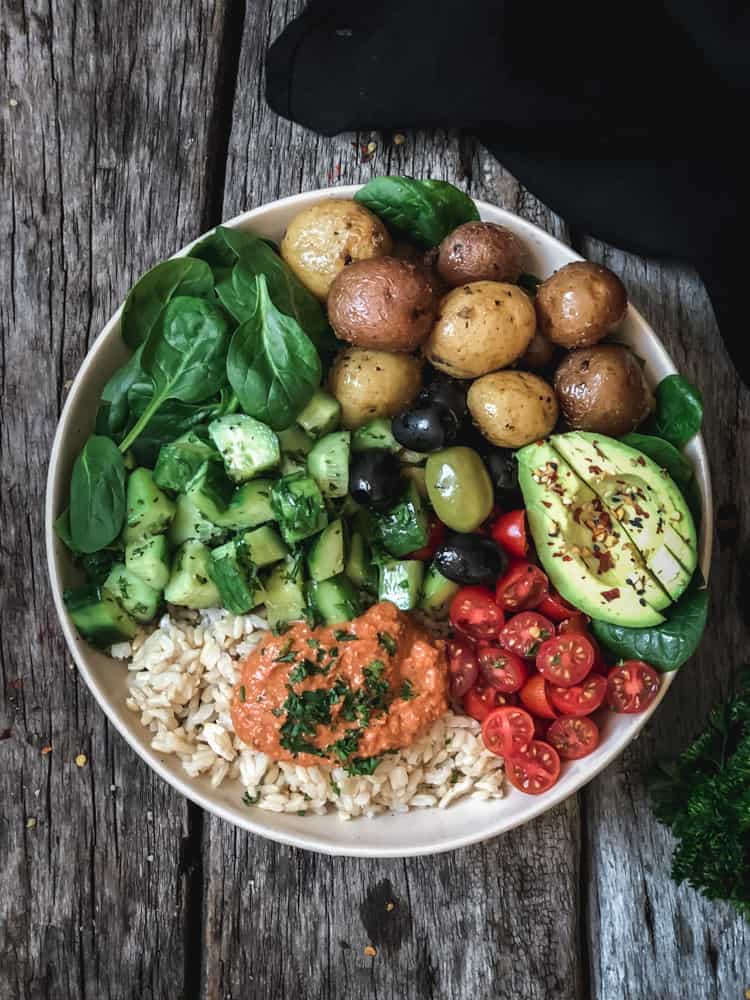 Vegan Buddha bowl made with Greek potatoes, avocado, olives, and harissa red pepper sauce.