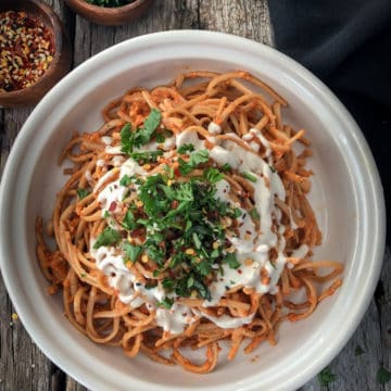 Bowlful of spaghetti with vegan roasted red pepper harissa sauce topped with a drizzle of cashew cream.