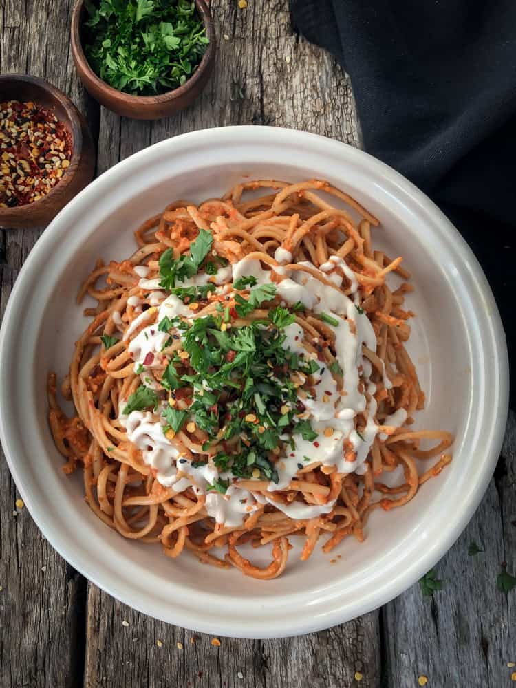 A bowlful of roasted red pepper harissa sauce on spaghetti pasta with a cashew cream drizzle and chopped parsley.