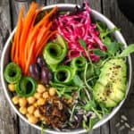 Bowl of green salad with carrots, avocados and beans.