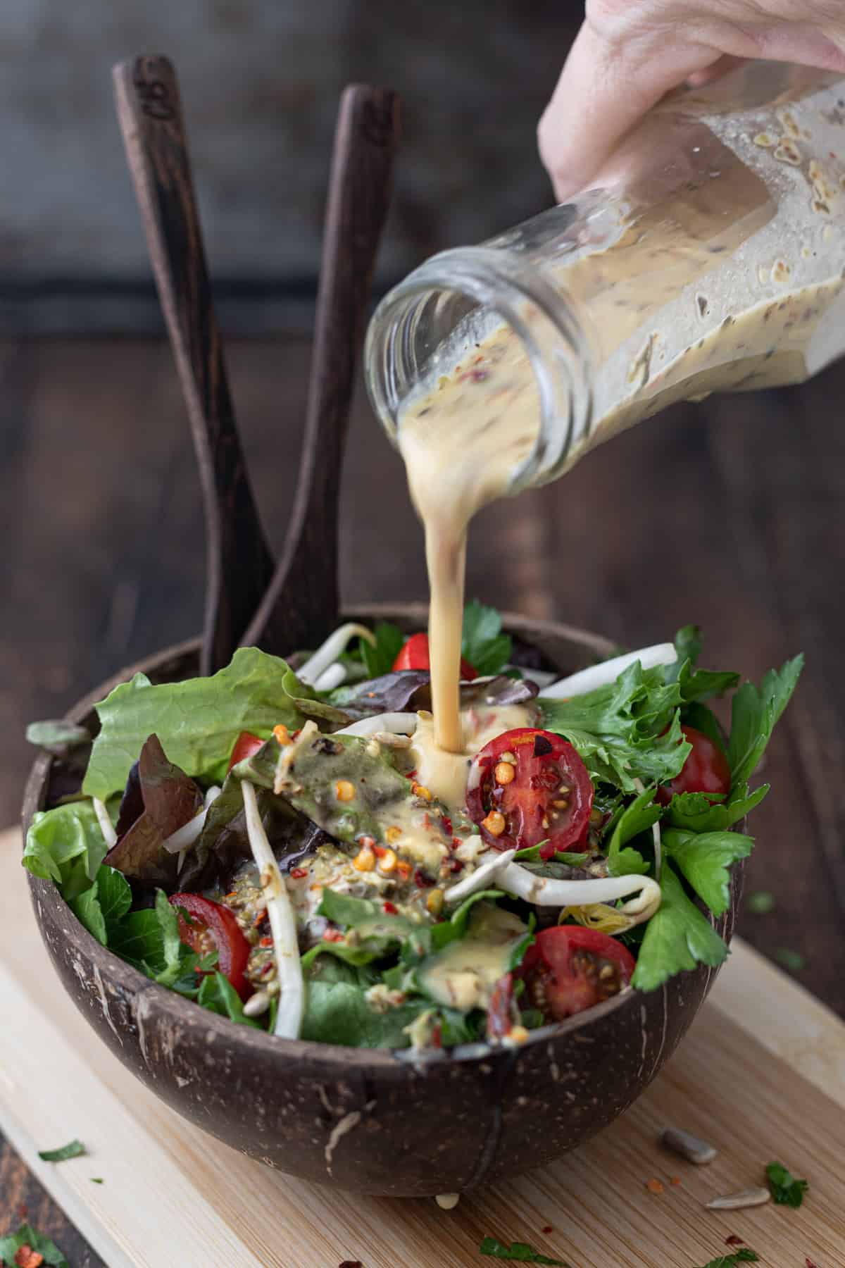 Dressing being poured onto a bowl of spring mix salad with tomatoes and sprouts.