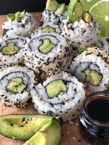 Vegan sushi made with avocado piled on a serving plate with a dish of soy sauce.