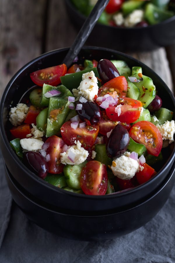Vegan Greek salad with feta cheese, tomatoes olives and greek salad dressing in a bowl.