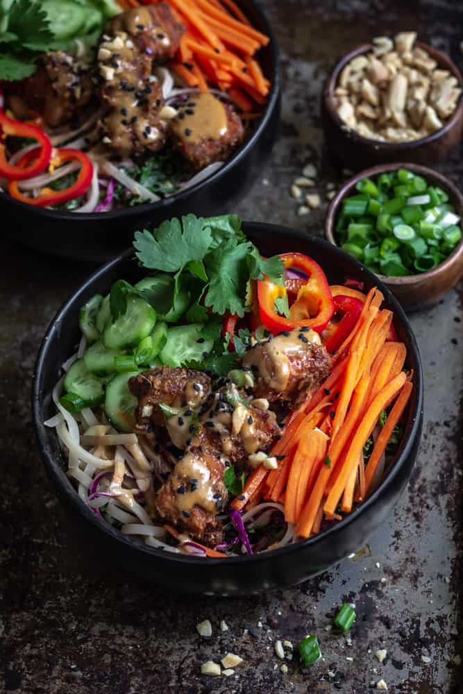 Spicy satay peanut tofu bowl with vegetables and rice noodles in a bowl.