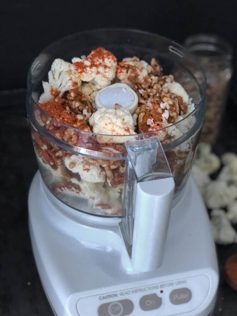Cauliflower, walnuts and spice in the bowl of a food processor.