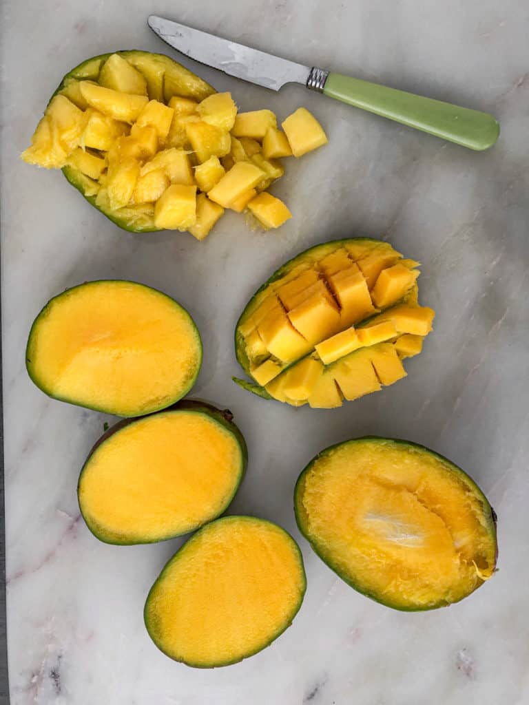 Sliced and chopped mangos on a cutting board with a knife.