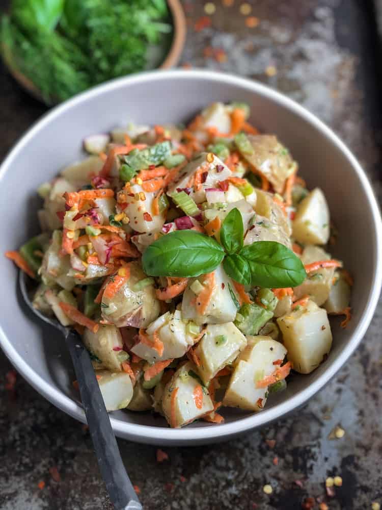 Bowl of vegan potato salad with carrots and basil.