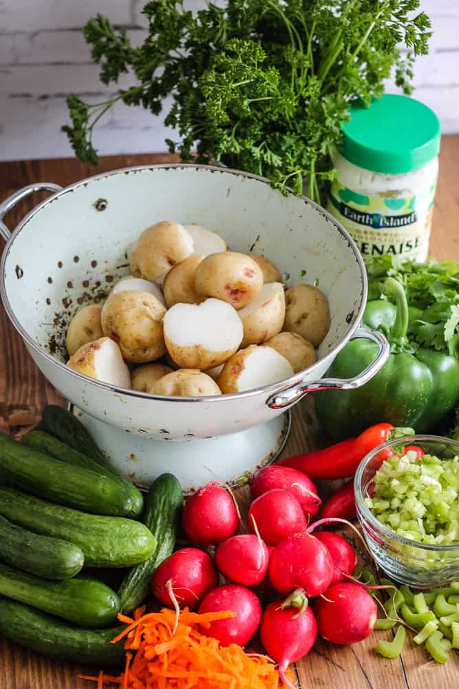 Fresh vegetable ingredients for vegan potato salad on a cutting board.