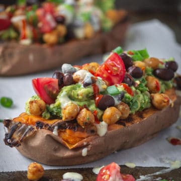 Baked sweet potatoes stuffed with guacamole, chickpeas, tomatoes, black beans with a spicy dairy-free sauce on top