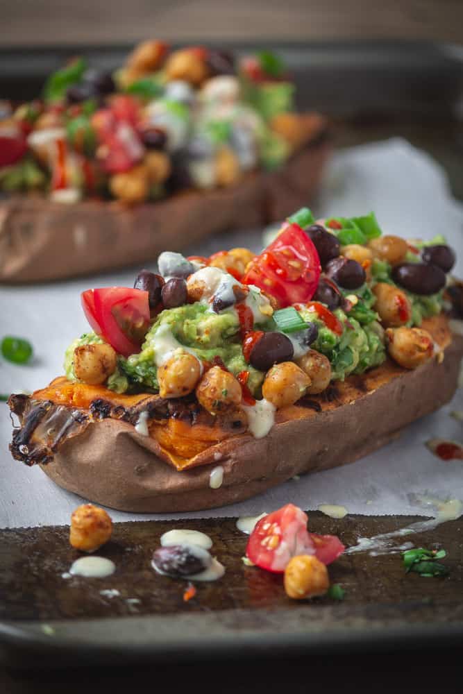 Baked sweet potato stuffed with beans, avocado and tomatoes on a baking sheet.