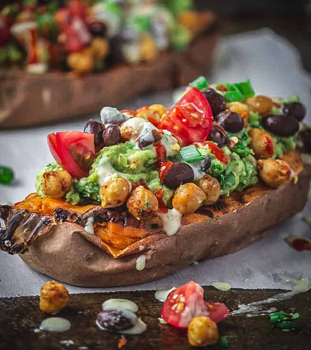 Sweet potato stuffed with black beans avocado and tomatoes on a baking sheet.