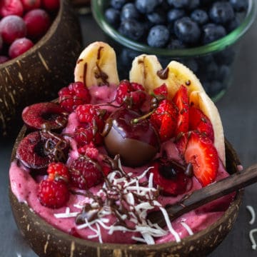 Vegan banana split with ice cream and fruit in a coconut bowl.