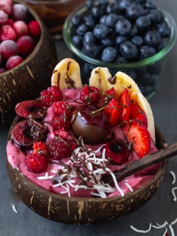 Vegan banana split with ice cream and fruit in a coconut bowl.